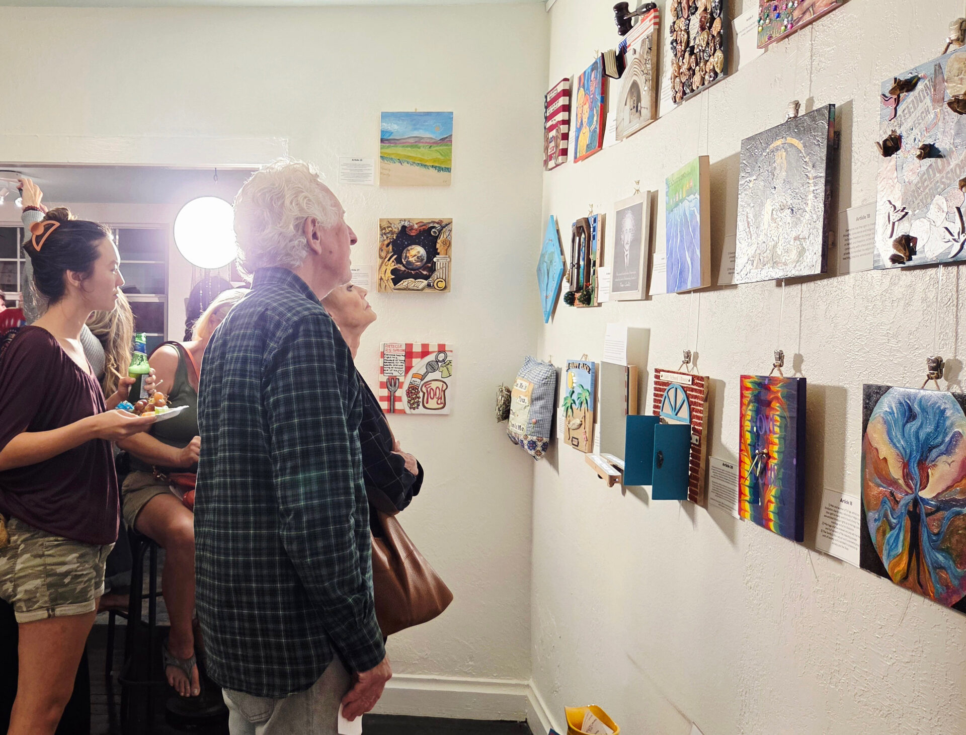 Gallery visitors admiring small mixed-media artworks displayed on the wall during an art show