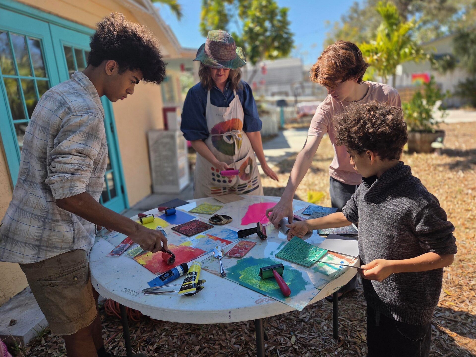 Teens and an instructor working on screen printing projects at an outdoor table