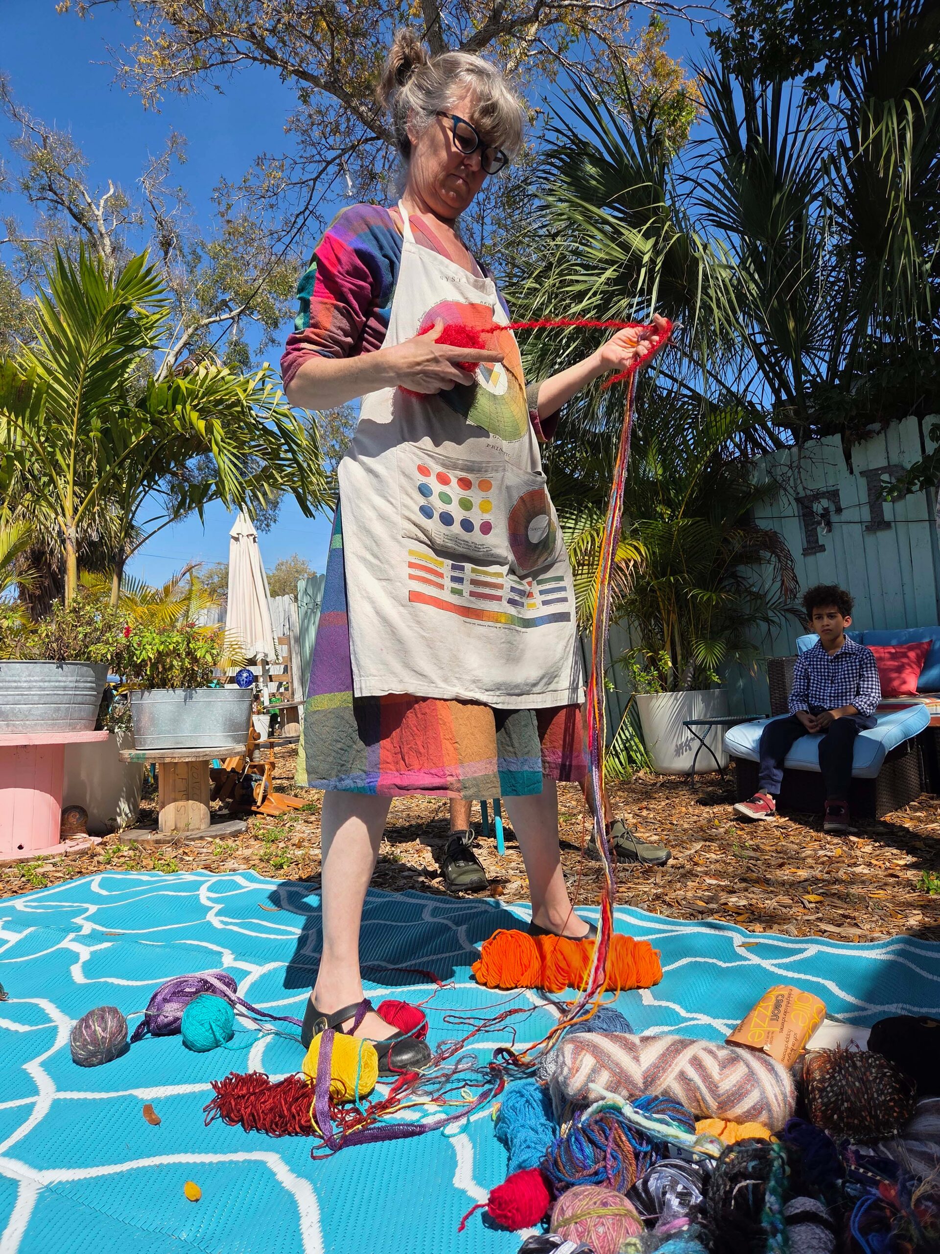 An instructor demonstrates yarn work outdoors during a fiber arts class in the garden