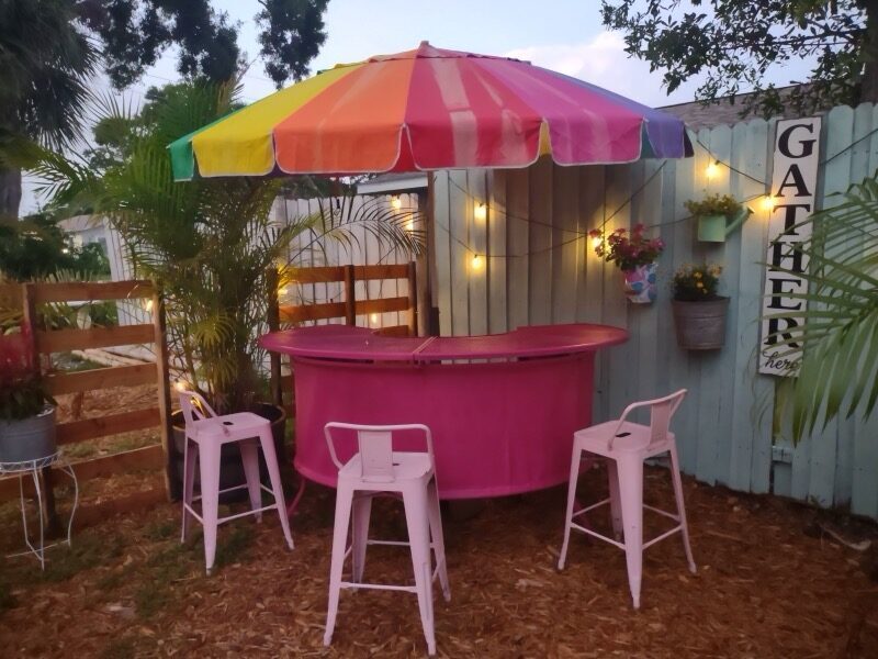 Pink outdoor bar with rainbow umbrella and string lights