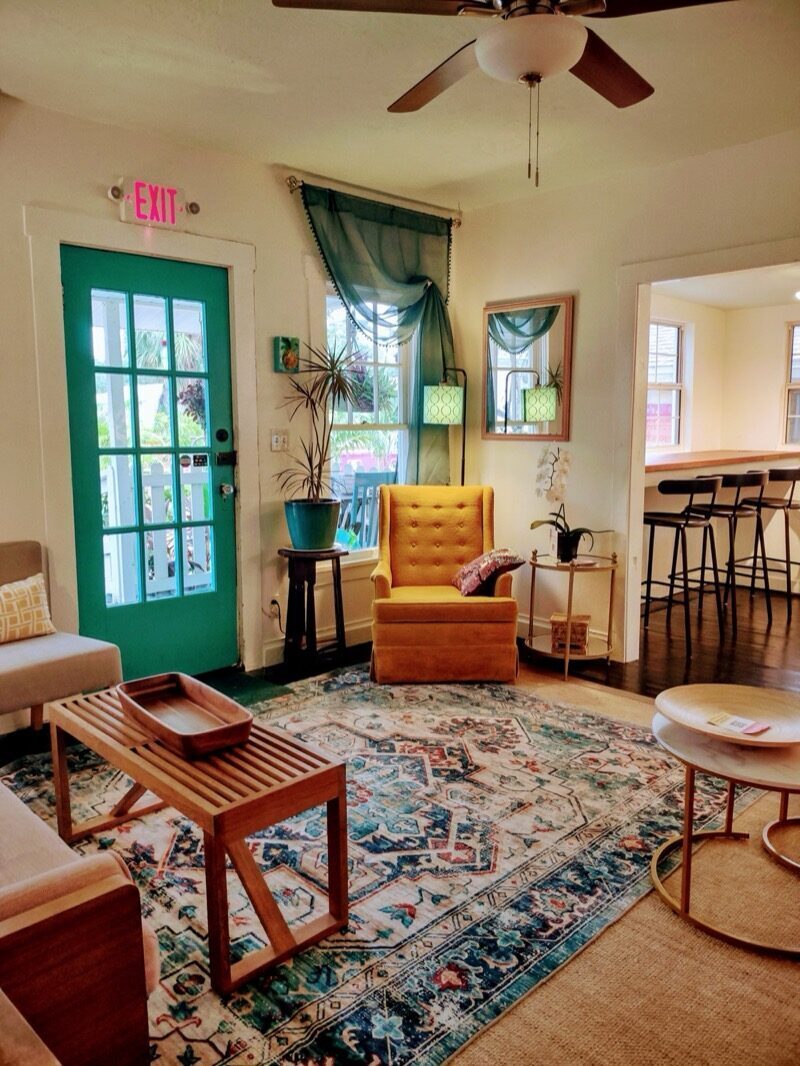 Sunlit living room with a mustard yellow chair and teal door